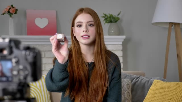 Young-red-haired-girl-blogger,-smiling,-talking-at-the-camera,-showing-a-new-purchase,-cosmetics,-lacquer,-make-up-concept,-home-comfort-in-the-background.-60-fps