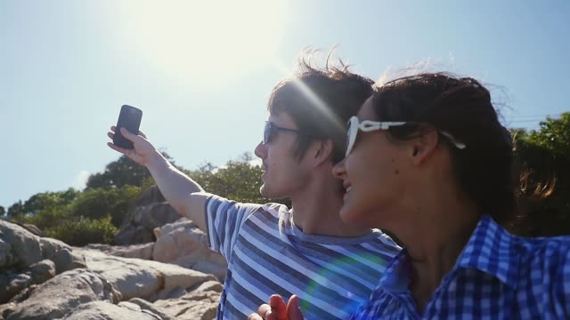 Young-couple-taking-selfie-portrait-by-beautiful-mountain-with-lense-flare-effects-and-the-sun-on-background-in-slow-motion.-1920x1080
