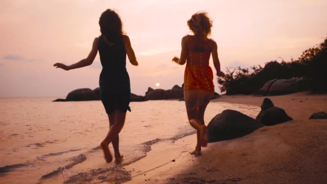 zwei-glückliche-Mädchen-laufen-ins-Wasser-bei-Sonnenuntergang-in-Zeitlupe