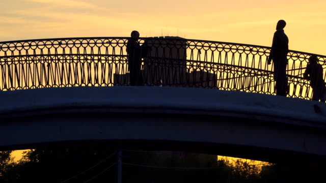 Silhouetten-von-Menschen,-die-Überquerung-des-Kanals-auf-eine-Bucklige-Brücke