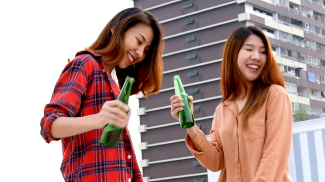 Junge-asiatische-Frau-lesbisches-Paar-Tanzen-und-klirrende-Flaschen-Bier-party-am-Dach.
