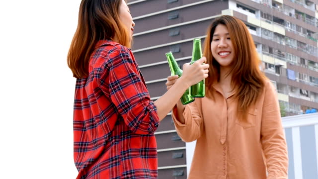 Mujer-asiática-joven-pareja-de-lesbianas-bailando-y-tintineantes-botellas-de-cerveza-fiesta-en-la-azotea.