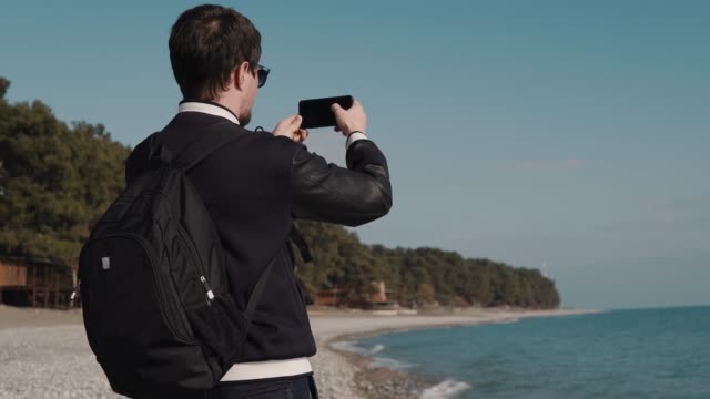 man-makes-a-series-of-photos-on-the-background-of-the-sea,-he-can-be-a-tourist