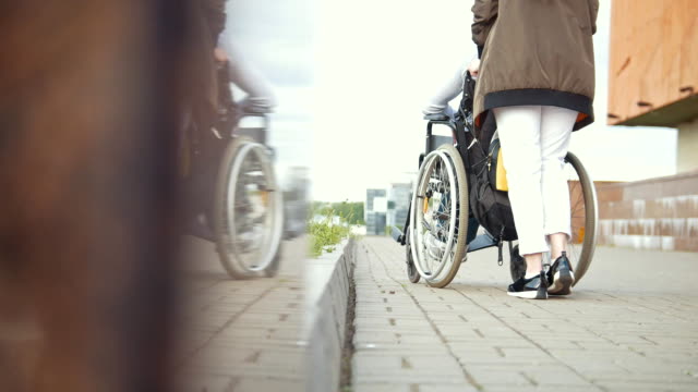 Young-woman-walking-with-disabled-man-in-a-wheelchair-down-the-street
