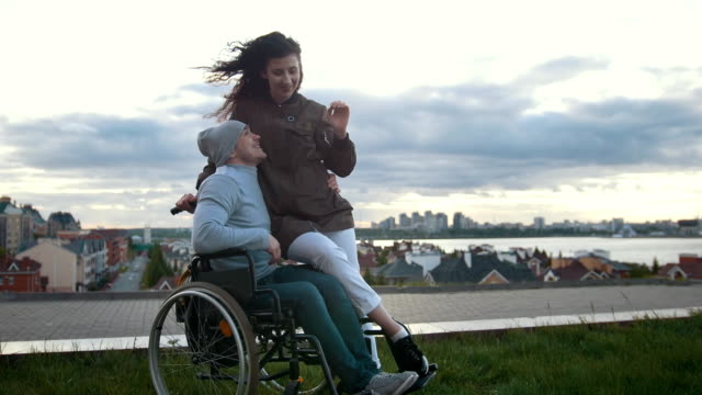 Happy-disabled-man-in-a-wheelchair-embraces-with-young-woman-outdoors