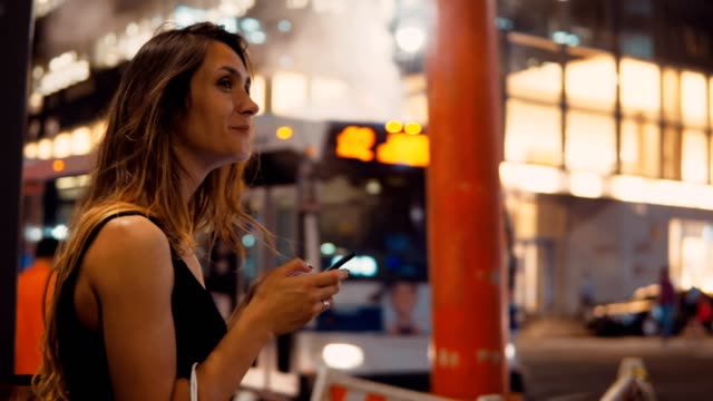 Mujer-joven-feliz-con-bolsas-de-pie-junto-a-la-pipa-de-humo-en-el-centro-de-tráfico-de-Nueva-York-y-el-uso-de-smartphone
