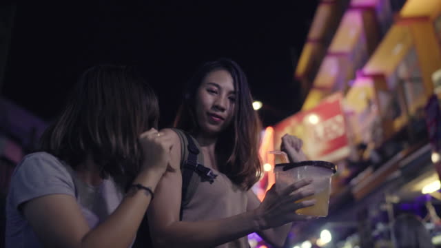 Slow-Motion---Reisende-Backpacker-asiatische-Frauen-Lesben-LGBT-Paare-tanzen-zusammen.-Weibliche-Alkohol-oder-Bier-mit-Freunden-trinken-und-feiern-auf-der-Khao-San-Road-in-Bangkok,-Thailand.