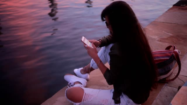 Mensajes-de-texto-de-mujer-joven-patinador-asiático-en-smartphone-por-el-mar