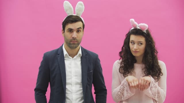 Young-beautiful-couple-standing-on-a-pink-background.-During-this,-they-are-dressed-in-rabble-ears.-Looking-gently-at-each-other,-in-love.