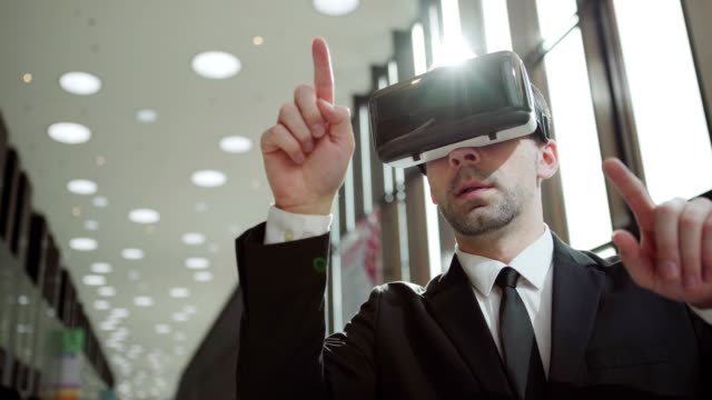 Modern-middle-aged-businessman-in-formal-suit-and-tie-wearing-VR-headset,-exploring-and-swiping-data-visualized-in-virtual-reality-in-sunlight