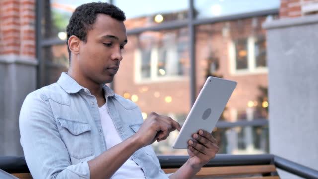 Afrikanischer-Mann-sitzt-im-Freien-und-benutzt-Tablet