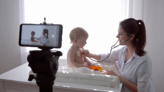 Online-Vortrag,-Blogger-Familienarzt-mit-Baby-untersuchte-wenig-Patient-mit-Stethoskop-und-führt-Live-Lernen-auf-dem-Handy-für-Anhänger