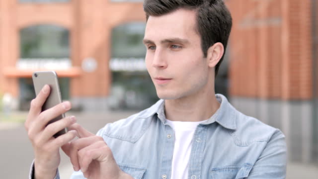 Outdoor-Young-Man-Celebrating-Success-on-Smartphone