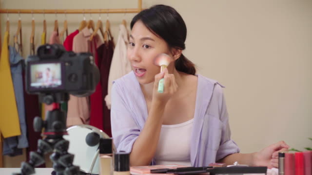Slow-motion---Beauty-blogger-present-beauty-cosmetics-sitting-in-front-camera-for-recording-video.-Happy-beautiful-young-Asian-woman-use-cosmetics-review-make-up-tutorial-broadcast-live-video.