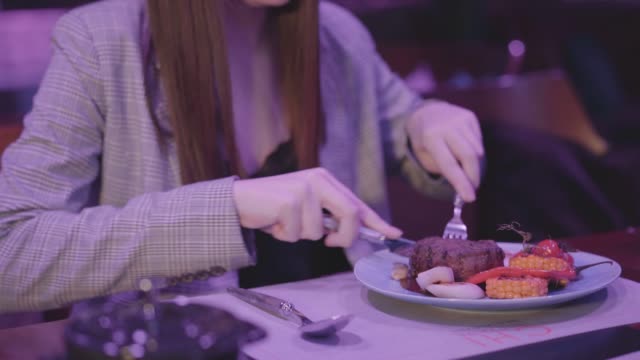 Cute-young-woman-eating-meat-grilled-with-vegetable-in-the-modern-restaurant.
