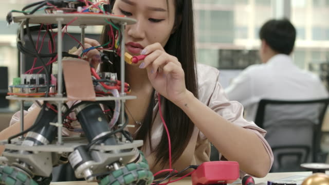 Asian-female-electronics-engineer-works-with-robot,-building,-fixing-robotics-in-workshop.-People-with-technology-or-innovation-concept.