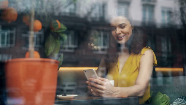 Lächelnde-junge-Frau,-die-auf-Smartphone-Bildschirm-während-schönen-Tag-im-Café