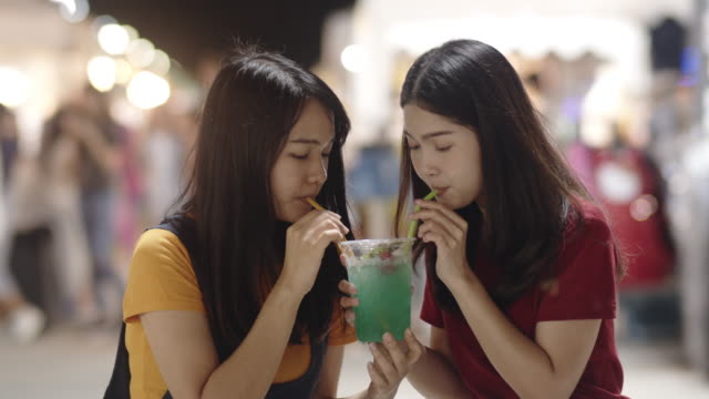 Asian-young-woman-friends-travel-in-Bangkok,-Thailand,-beautiful-female-feeling-happy-drinking-cocktail-at-The-Khao-San-Road.-Women-travel-eat-street-food-in-Thailand-concept.-Slow-motion-shot.