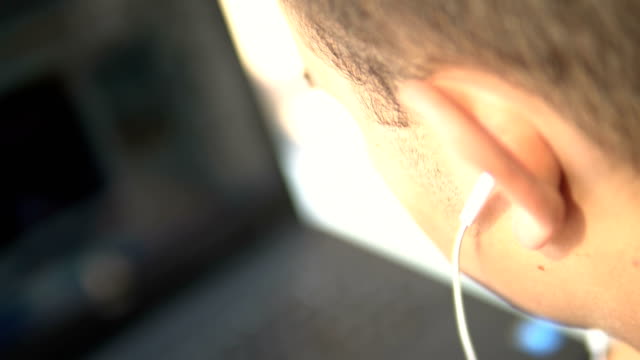 Guapo-hombre-adolescente-con-auriculares-viendo-película-en-la-computadora-portátil,-enfoque-selectivo-cinematográfico