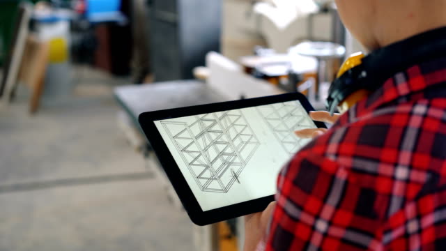 Carpintero-usando-tableta-en-taller-mirando-el-diseño-de-muebles-en-pantalla