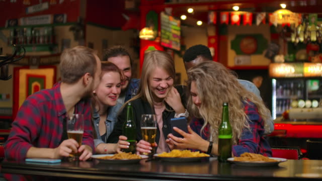 Eine-große-Gruppe-von-Freunden-in-der-Bar-sitzt-am-Tisch-lachend-und-plaudert-Bier-trinken