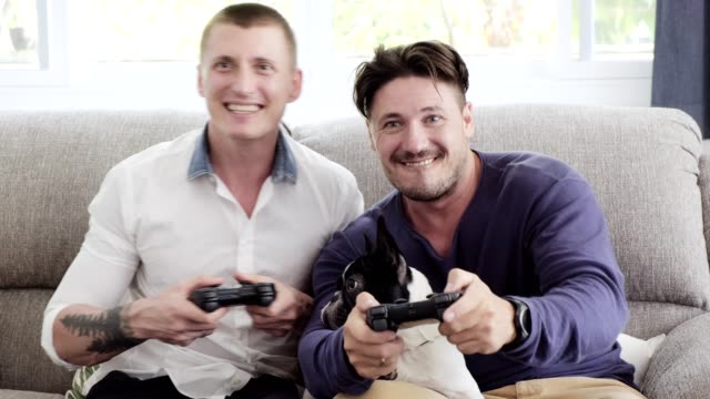 Gay-couple-relaxing-on-couch-with-dog-playing-games.-Enjoy-gaming-session.