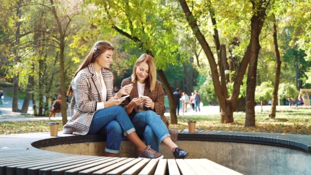 Glückliche-Mädchen-surfen-Social-Media-mit-Smartphones-in-öffentlichen-Park