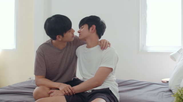 Asiatische-Homosexuell-Paar-küssen-auf-dem-Bett-zu-Hause.-Junge-asiatische-LGBTQ-Männer-glücklich-entspannen-sich-zusammen-verbringen-romantische-Zeit-nach-dem-Aufwachen-im-Schlafzimmer-zu-Hause-im-Morgen-Konzept.-Zeitlupe-Schuss.