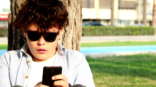 Teenage-boy-sitting-at-the-outdoor-with-smartphone