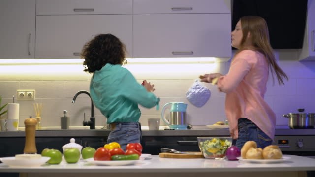 Positive-sisters-moving-to-music-dancing-together-in-kitchen,-having-fun-at-home