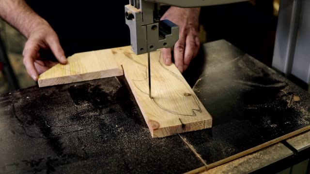 Close-up-footage-of-male's-hands-working-with-an-electric-cutting-machine.-High-angle-footage-of-a-man-cutting-a-fish-shape-wooden-pattern-on-a-table