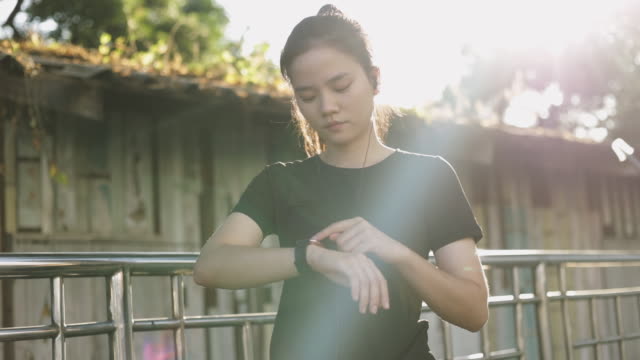 Attraktive-junge-asiatische-Sportlerin,-die-mit-Herzfrequenz-auf-einer-Smartwatch-checkt.-Jogging-Workout-Lifestyle-auf-der-Straße-bei-Sonnenuntergang.