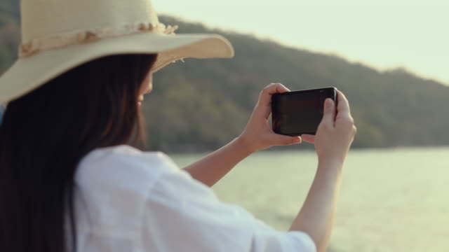 Glückliche-asiatische-Teenager-Frau-hält-Smartphone,-das-ein-Foto-am-Strand-schönen-Sonnenuntergang.-Lifestyle-Reise-Urlaub-Urlaub-Sommerkonzept.