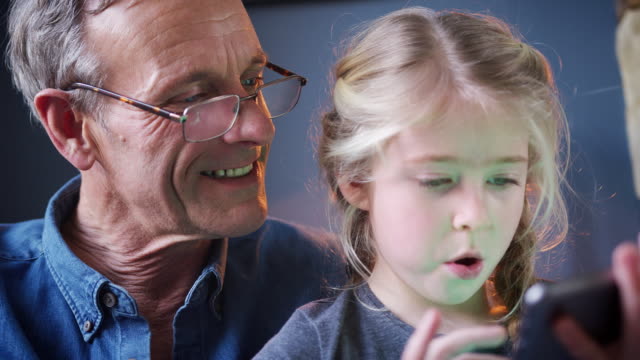 Nahaufnahme-von-Enkelin-mit-Großvater-im-Stuhl-spielen-auf-digitalen-Tablet-zu-Hause-zusammen