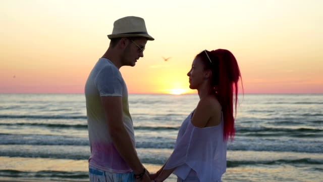 Romantisches-Paar-Hand-in-Hand-und-Blick-auf-den-Horizont-am-Strand-bei-Sonnenuntergang