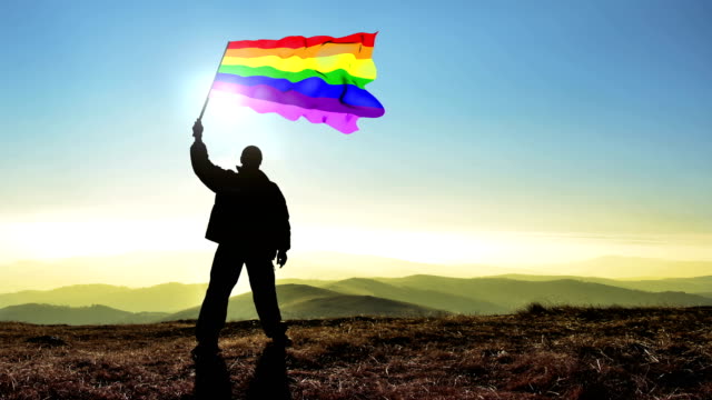 Erfolgreiche-Silhouette-Mann-Sieger-winken-Gay-Homo-Flagge-oben-auf-der-Bergspitze,-4-k-Cinemagramm