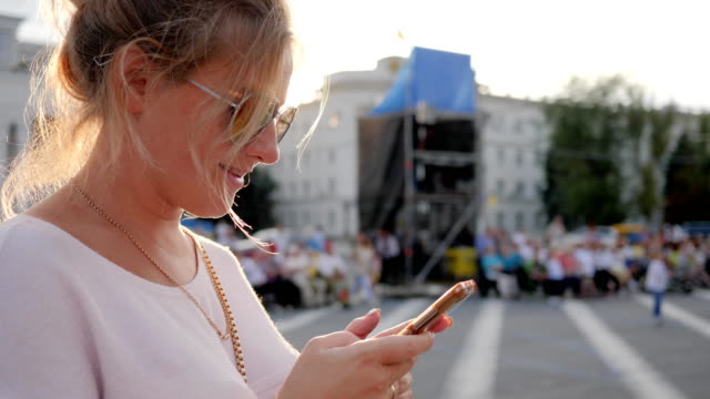 süße-Frauen-in-Gläser-hält-Smartphone-in-Händen-und-lächelte-im-freien-Innenstadt-in-Sonnenstrahlen