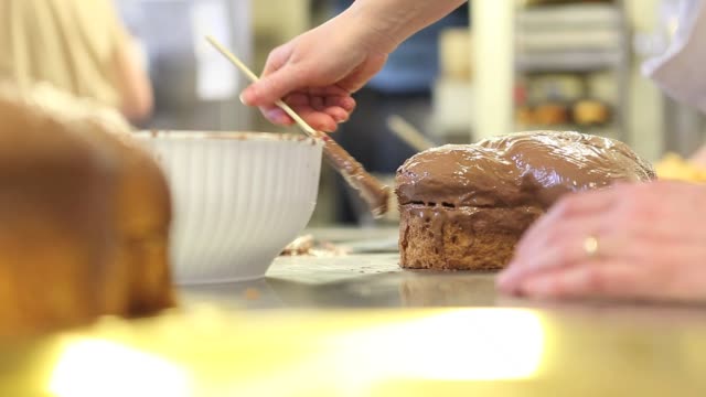 pastry-chef--hands-glazed-Easter-sweet-bread-cakes-with-chocolate,-closeup-on-the-worktop-in-confectionery