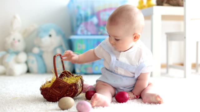 Niedlichen-Kleinkind-Kleinkind,-Baby-Boy,-im-sonnigen-Wohnzimmer-spielen-mit-Schokolade-Osterhasen-und-bunte-Ostereier
