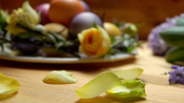 Petals-of-rose-fall-on-a-table-against-a-background-of-colored-Easter-eggs