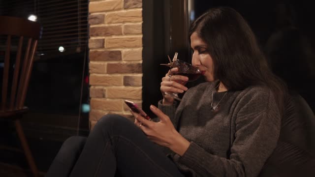 Eine-junge-Frau-sitzt-auf-einem-Stuhl-Kissen-in-einem-Café-und-trinkt-einen-cocktail