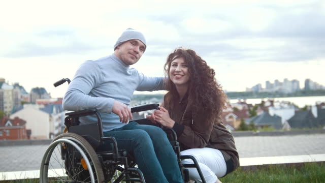 Retrato-de-un-feliz-hombre-discapacitado-en-silla-de-ruedas-abraza-con-joven-al-aire-libre