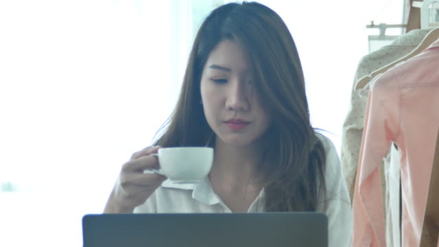 Bella-mujer-sonriente-joven-trabajando-en-ordenador-portátil-mientras-disfruta-de-beber-café-caliente-sentado-en-una-sala-de-estar-en-casa.-Disfrutando-en-casa.-Mujer-de-negocios-asiáticos-trabajando-en-su-oficina-en-casa.
