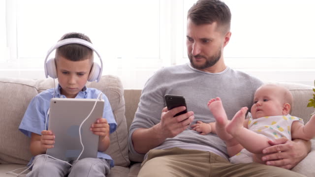 Young-family-sitting-on-couch-and-using-gadgets