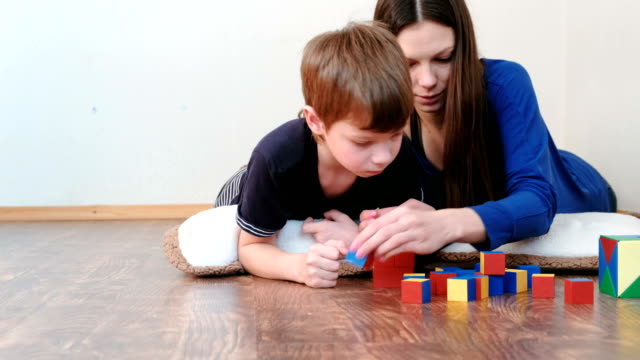 Madre-e-hijo-jugando-juntos-educación-color-madera-juguete-de-bloques-en-el-suelo.-Construyen-un-cuadro-rojo.