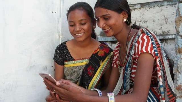 Zwei-indische-Mädchen-in-einem-Dorfhaus-im-ländlichen-Indien-Teilen-Lachen-auf-Handy-vorwärts-video-Witz-Emoji-Foto-auf-ihren-Touch-Bildschirm-lustige-witzige-voll-besetzten-lachen-Unternehmen-Teamarbeit-Verklebung