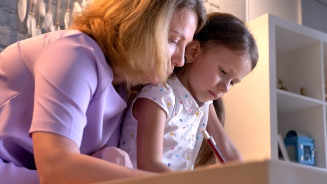 Kaukasische-Mutter-Hausaufgaben-mit-ihrer-Tochter,-Kind-mit-Studie-zu-helfen,-an-modernen-Zuhause,-Familie-Konzept-drinnen-sitzen