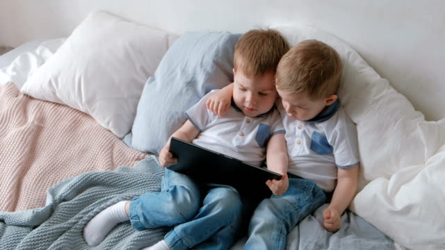 Kids-with-tablet.-Two-boys-twins-toddlers-looking-cartoon-at-tablet-lying-on-the-bed.