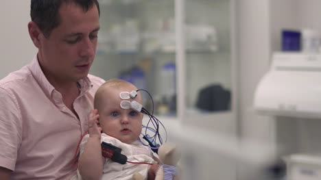 Papa-hält-ein-Baby-mit-medizinischen-Sensoren-an-Händen
