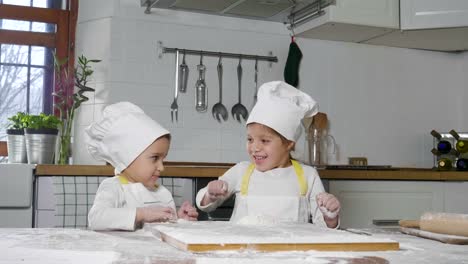 Two-little-girls-in-the-kitchen-prepare-food,-a-dessert-for-the-family.-As-they-learn-to-cook-they-start-playing-with-flour-and-smiling-each-other.